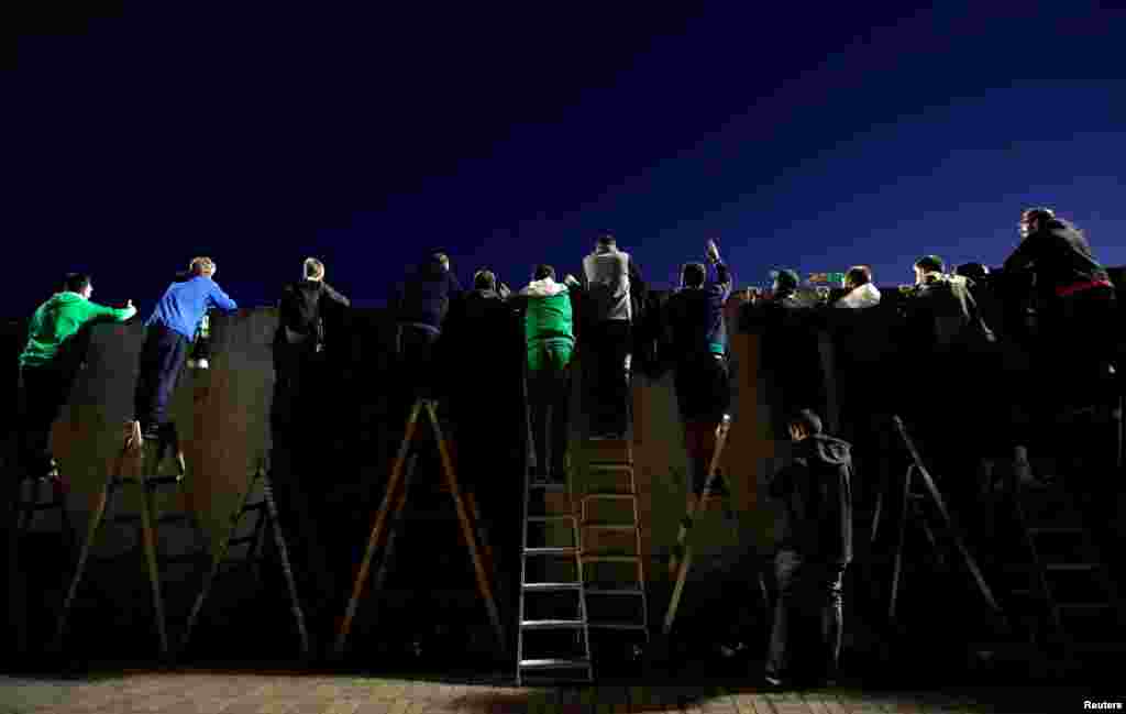 Fans standing on ladders behind a wall watch a match of the Czech top-tier soccer competition between Bohemians Prague and Sparta Prague as the match is closed for spectators due to the measures taken to curb the coronavirus disease (COVID-19) outbreak.