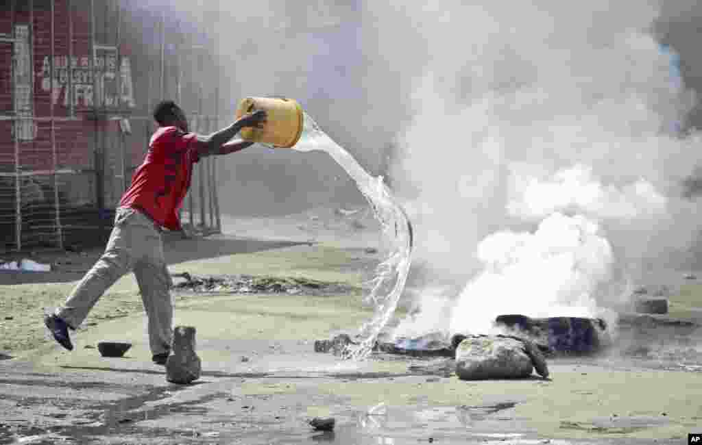 A man throws a bucket of water to put out flames from a tire set on fire in a street by rioting youths, Mombasa, Kenya, Oct. 4, 2013. 