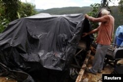 Moises Perez looks at some of his belongings covered by a tarpaulin, outside his home in Naguabo, Jan. 26, 2018.