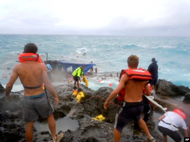 FILE - People clamber on Christmas Island during a rescue attempt as a boat breaks up in the background, Dec. 15, 2010. The boat, packed with dozens of asylum-seekers, smashed apart on cliff-side rocks in heavy seas, sending some to their deaths.