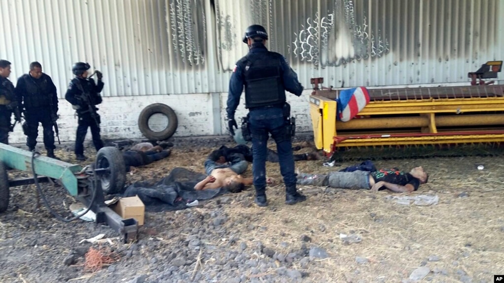 FILE - Federal police stand near the bodies of men who authorities say were suspected cartel gunmen at the Rancho del Sol, near Ecuanduero, in western Mexico.