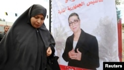 FILE - A women walks past electoral posters of Louisa Hanoune, a candidate for Algeria's Workers' Party in the 2014 presidential election, March 27, 2014.