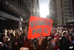 Kelly Crowder, center, holds up a sign as thousands of protesters gather for the Women's March against President Donald Trump, Jan. 21, 2017, in Los Angeles.