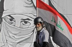 An Iraqi protester carrying his national flag walks past graffiti during ongoing anti-government protests, at Tahrir square in the capital Baghdad.