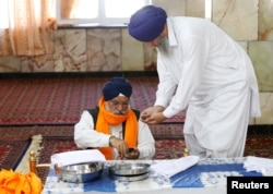 An Afghan Sikh (R) receives karah prasad, a sweet pudding offering given out to a congregation at the end of prayer, inside a Gurudwara, or a Sikh temple, during a religious ceremony in Kabul, Afghanistan, June 8, 2016.