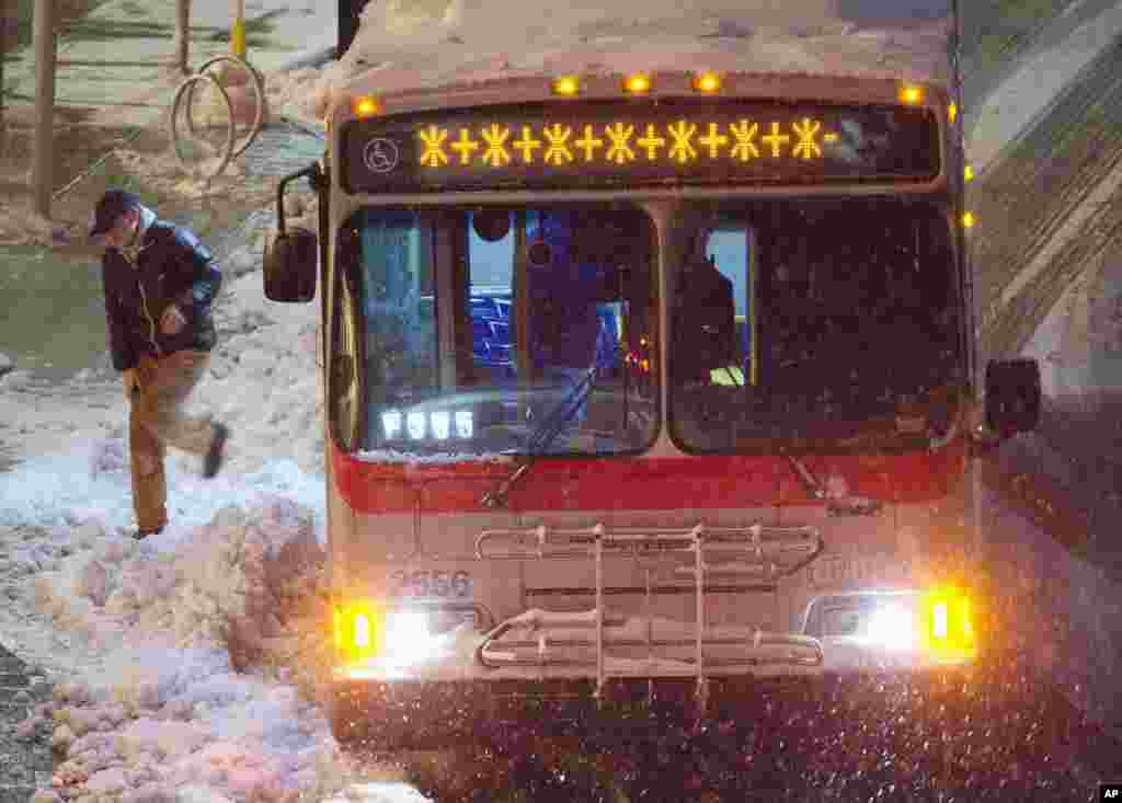 A commuter steps through the snow by a Metro bus, early Monday morning, Arlington, Virginia, March 17, 2014.