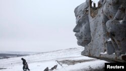 A man and a child walk in the snow at the destroyed war memorial at Savur-Mohyla, a hill east of the city of Donetsk, Dec. 7, 2014.