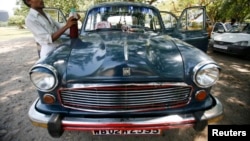 A driver stands next to his parked Ambassador car, manufactured by Hindustan Motors, 