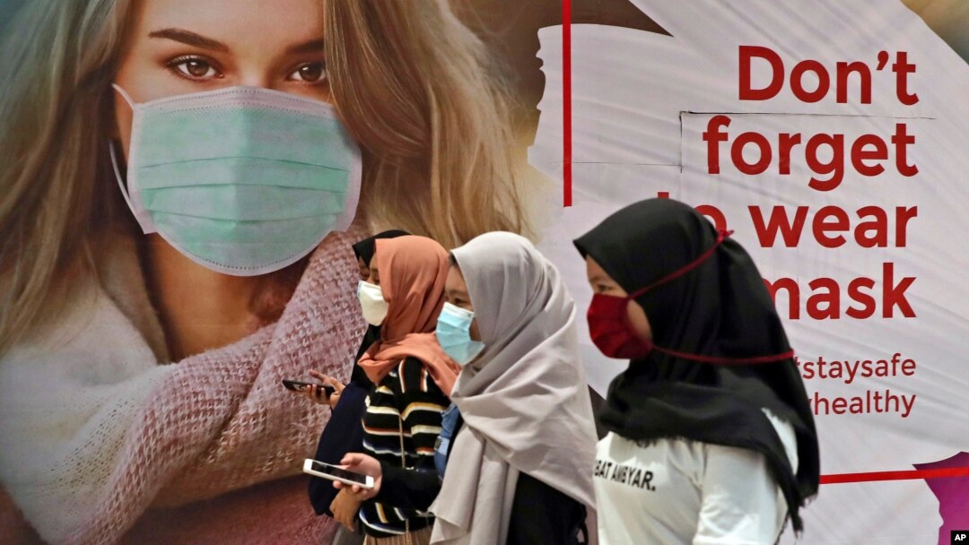 Perempuan mengenakan masker melewati poster promosi kesadaran pandemi Covid-19 di sebuah pusat perbelanjaan di Jakarta, 1 Juli 2020. (Foto: dok).