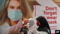 Women wearing protective face masks walk by an advertisement promoting awareness of the coronavirus outbreak at a shopping mall in Jakarta, Indonesia, July 1, 2020.