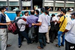 FILE - Commuters ignoring physical distancing norms push each other as they try to board on a long distance bus in Kolkata, India, Oct. 1, 2020.
