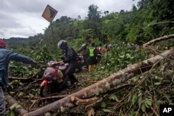 Sejumlah pengendara motor melewati jalan yang rusak akibat tanah longsor yang dipicu gempa dekat Mamuju, Sulawesi Barat, Sabtu, 16 Januari 2021.(Foto: AP)
