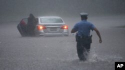 Policajac u Filadefliji priskače u pomoć vozaču putničkog automobila za vreme naleta tropske oluje Isaias (Foto: AP)