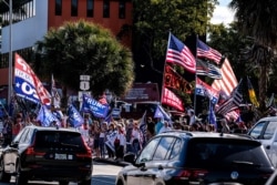 Supporters of former U.S. President Donald Trump hold signs and wave flags as they stand along the route of his motorcade in West Palm Beach, Florida, Jan. 20, 2021.