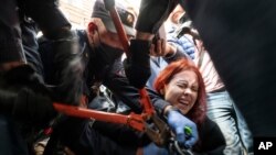 Police try to cut the cuffs off a woman who had handcuffed herself to a fence during a rally supporting Khabarovsk region's governor, Sergei Furgal, in St. Petersburg, Russia, Aug. 1, 2020. Crowds rallied in Khabarovsk as well for a yet another weekend.