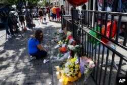 A mourner kneels at a makeshift memorial near members of the media outside the Hole in the Wall bar in the Oregon District in Dayton, Ohio, Aug. 5, 2019.