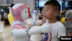 FILE - A boy stands next to an iPal robot at Avatarmind's booth at the World Robot Conference (WRC) in Beijing, China,.