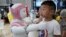 FILE - A boy stands next to an iPal robot at Avatarmind's booth at the World Robot Conference (WRC) in Beijing, China,.