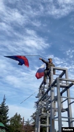 A member of the Ukrainian troop brings down a Donetsk Republic flag hoisted on a monument in Lyman