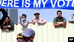 Cambodian workers look through a partition of a construction site below a banner which reads "Where is my vote" as supporters of opposition Cambodia National Rescue Party gather in Phnom Penh, file photo. 