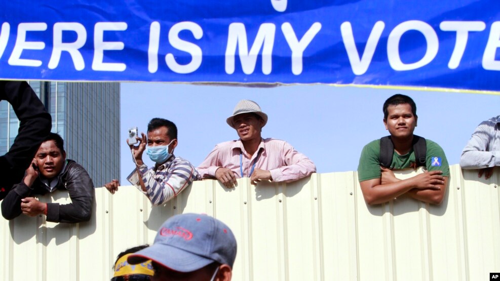  Cambodian workers look through a partition of a construction site below a banner which reads "Where is my vote" as supporters of opposition Cambodia National Rescue Party gather in Phnom Penh, Cambodia, Saturday, Sept. 7, 2013.