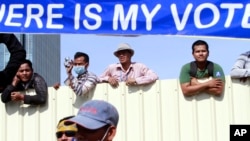 Cambodian workers look through a partition of a construction site below a banner which reads "Where is my vote," file photo. 