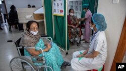 A woman receives the COVID-19 vaccine as another waits in a wheelchair at a private hospital in Gauhati, India, March 4, 2021.
