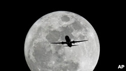 FILE - A commercial airliner crosses the first full Moon of the year, called the Wolf Moon over Whittier on its way to Los Angeles Airport, Jan. 4, 2015.