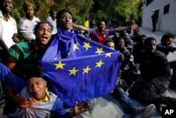 FILE - A migrant holding a European Union flag sits on the ground with others after storming a fence to enter the Spanish enclave of Ceuta, Spain, February 17, 2017.