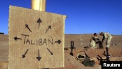 资料照片：在阿富汗南部，美国海军陆战队员在美国海军陆战队基地的前线填充沙袋，附近有一个纸板标志，提醒大家塔利班可能在任何地方（2001年12月1日）。
