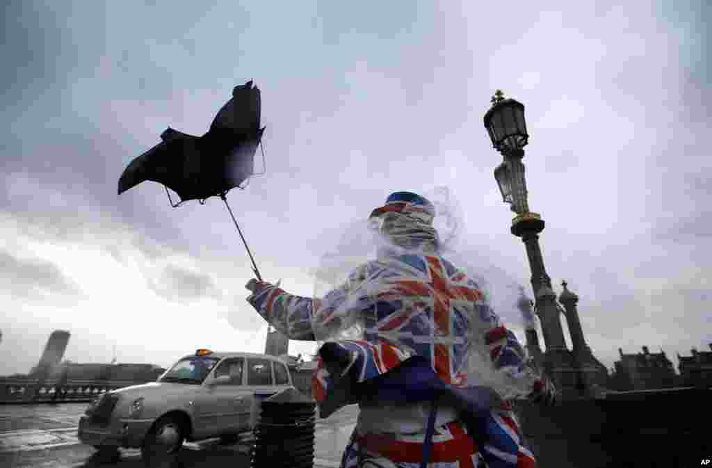 A man giving out leaflets to tourists is blown by the wind in Westminster in London. Winds of nearly 100mph battered Britain after another storm slammed into the south coast bringing fierce gusts and torrential downpours.