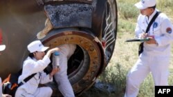 Retrieval team members collect a sample from the charred return capsule of the Shenzhou-9 spacecraft in a remote area of northern China, June 29, 2012.