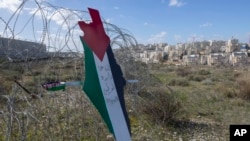 Protesters post a placard with the colors of the Palestinian flags and Arabic that reads "Jerusalem is the eternal capital of Palestine," at a barbed wire surrounding the Israeli separation wall and an Israeli settlement near Ramallah, Jan. 31, 2020.