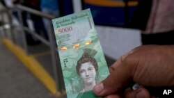 Una persona muestra un billete de 5.000 Bolívares afuera de un banco en Caracas, Venezuela. El presidente Nicolás Maduro anunció el retiro del actual cono monetario por uno nuevo que comenzará a regir en junio.