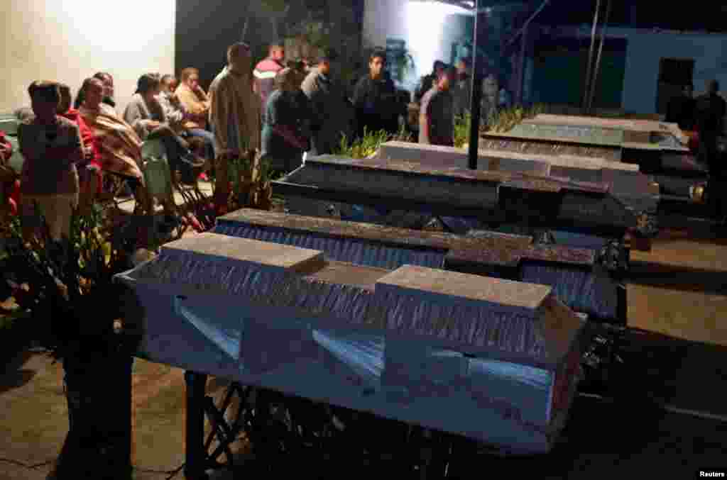 People stand next to caskets holding the bodies of victims who died after the roof of a church collapsed, after an earthquake hit Atzala, on the outskirts of Puebla, Mexico, Sept. 20, 2017.
