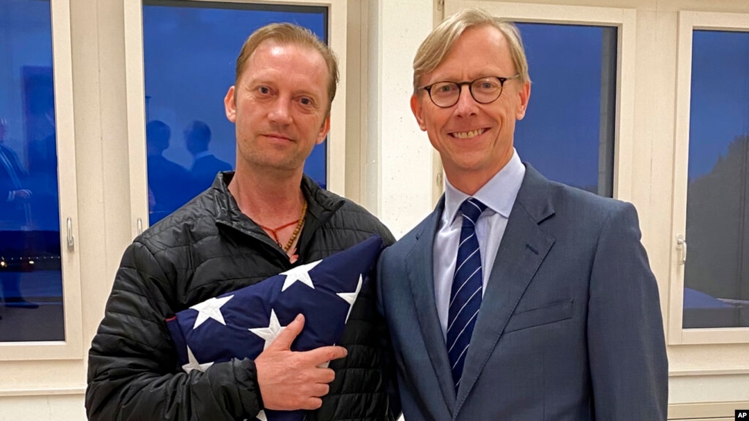 FILE - In this image provided by the U.S. State Department, Michael White holds an American flag as he poses for a photo June 4, 2020, with U.S. special envoy for Iran Brian Hook at the Zurich, Switzerland, airport after White’s release from Iran.