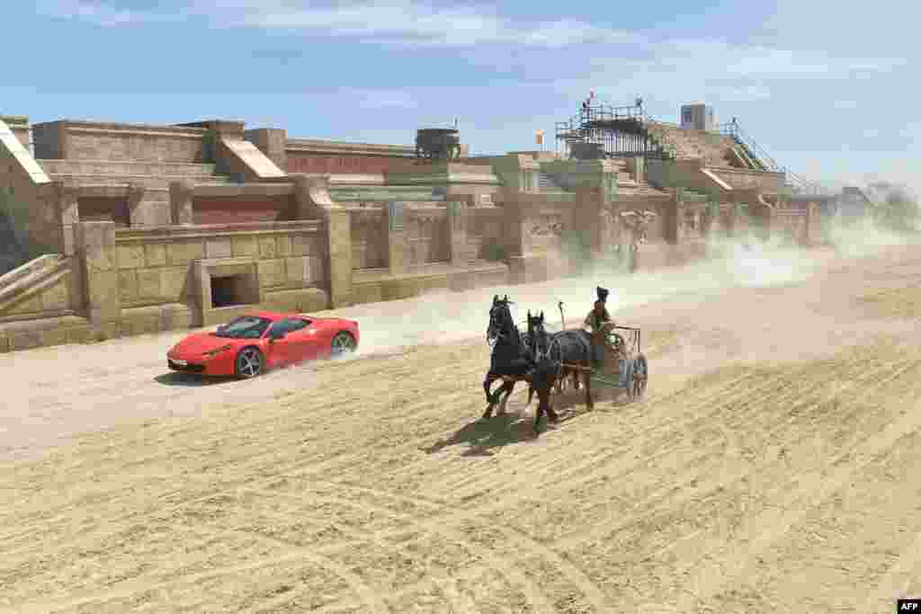 Ferrari driver Fabio Barone and his Ferrari 458 Italia compete against a Roman chariot drawn by two horses on "Ben Hur" movie set at Cinecitta World amusement park in Castel Romano near Rome, Italy.