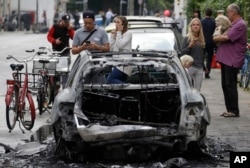 Un auto quemado por manifestantes es observado por varias personas en Hamburgo, Alemania, en el primer día de la Cumbre del G20. Julio 7 de 2017.