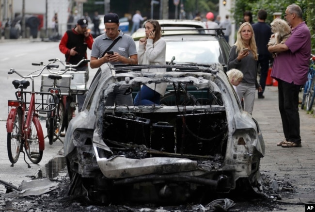 Un auto quemado por manifestantes es observado por varias personas en Hamburgo, Alemania, en el primer día de la Cumbre del G20. Julio 7 de 2017.