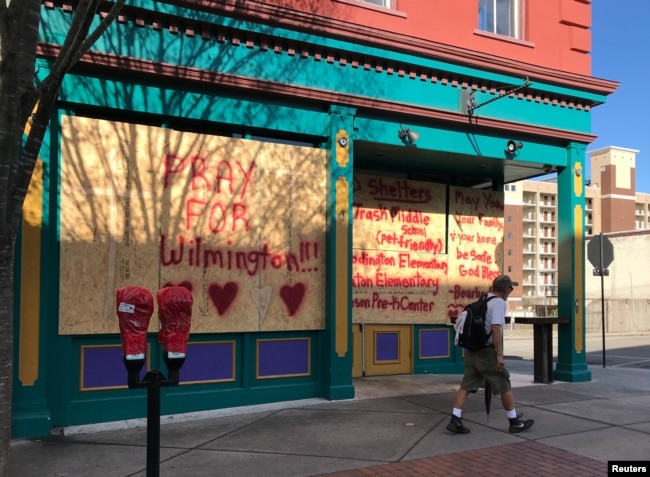 A man passes graffiti reading "Pray for Wilmington" on a business boarded up for the arrival of Hurricane Florence in Wilmington, North Carolina, Sept. 12, 2018.