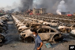 A man walks past the charred remains of new cars at a parking lot near the site of an explosion at a warehouse in northeastern China's Tianjin municipality, Aug. 13, 2015.
