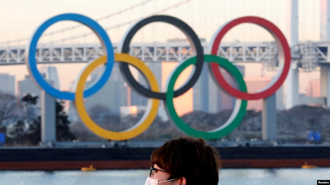 FILE - A man wears a protective mask amid the coronavirus (COVID-19) outbreak in front of the giant Olympic rings in Tokyo, Japan, Jan. 13, 2021. 