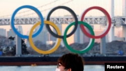 FILE - A person wears a protective mask amid the coronavirus outbreak in front of the giant Olympic rings in Tokyo, Japan, Jan. 13, 2021.