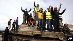 Anti-government protesters make victory signs as they stand on an army tank in Benghazi, February 24, 2011