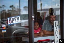 A man and girl peer out from a bakery and cafeteria in Freeport, Bahamas, Wednesday, Sept. 11, 2019. Those who survived Hurricane Dorian are facing the prospect of starting their lives over but with little idea of how or where to even begin. (AP Photo/Ram