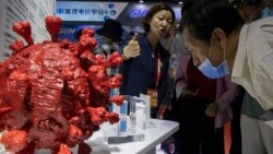 An employee answers questions from the public near samples of a COVID-19 vaccine produced by Sinopharm subsidiary CNBG are displayed during a trade fair in Beijing on Sunday, Sept. 6, 2020