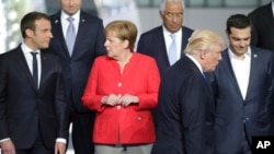 FILE - French President Emmanuel Macron, left, speaks with German Chancellor Angela Merkel, second left, as U.S. President Donald Trump walks to take his position during a group photo at the new NATO headquarters in Brussels on Thursday, May 25, 2017.