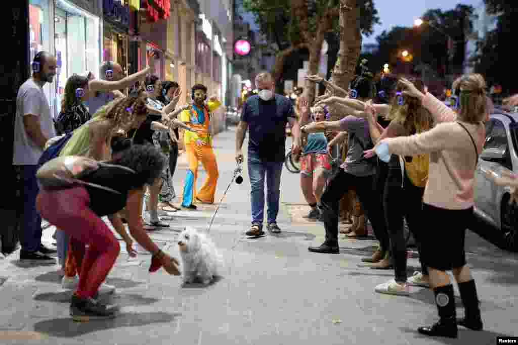 A man wears a mask and walks his dog past people taking part in a silent disco event as some businesses reopened at the end of last month following weeks of shutdown amid the coronavirus disease (COVID-19) crisis, in Tel Aviv, Israel.