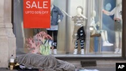 A homeless person sleeps in front of a closed clothing shop in London, Thursday May 14, 2020, 