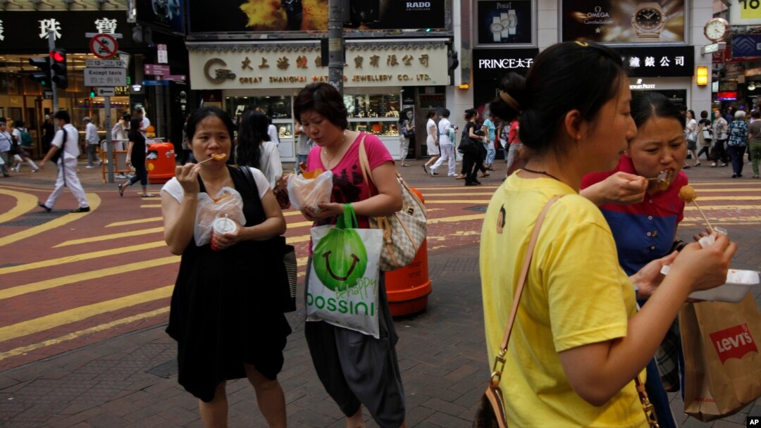 Para turis dari China daratan memakan jajanan pinggir jalan di pusat kota Hong Kong. (Foto: Dok)